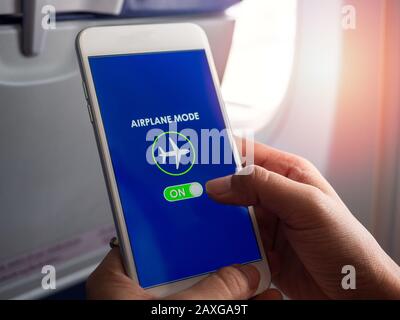 Flight mode concept. Close-up finger sliding on screen for turned on airplane mode near the window on the airplane. Stock Photo