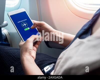 Flight mode concept. Hand holding white smartphone and turned on airplane mode on screen near the window on the airplane. Stock Photo