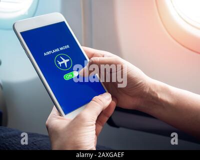 Flight mode concept. Finger sliding on screen for turned on airplane mode near the window on the airplane. Stock Photo