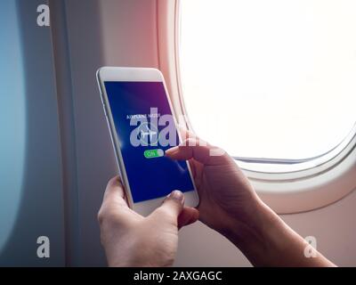Flight mode concept. Finger sliding on screen for turned on airplane mode near the window on the airplane with copy space. Stock Photo