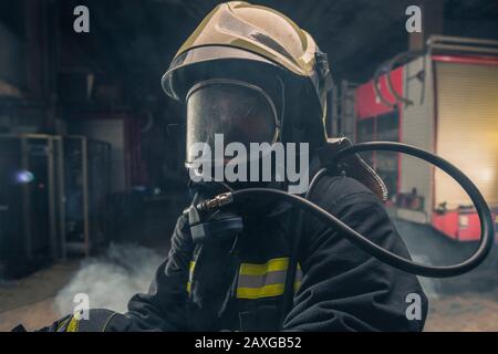 Portrait of a fireman wearing firefighter turnouts and helmet. Dark background with smoke and blue light. Stock Photo