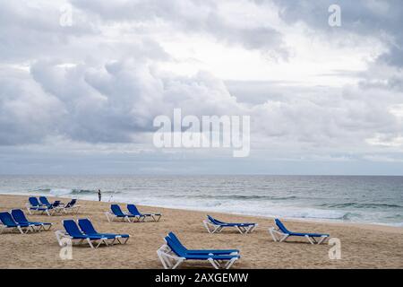 Tavira, Portugal - January 23, 2020: One senior fisherman casts his pole and line out during the rough seas of winter. Empty blue beach chairs in fore Stock Photo