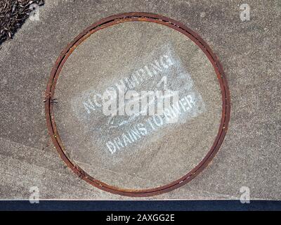 A manhole cover over a drain on the side of a street with a fish picture on it says NO DUMPING DRAINS TO RIVER in Santa Rosa, California. Stock Photo