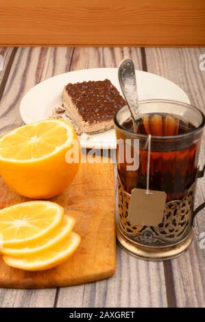 Tea in a faceted glass in a vintage Cup holder, sliced lemon on a Board and a piece of waffle cake on a white plate on a wooden background. Close up Stock Photo