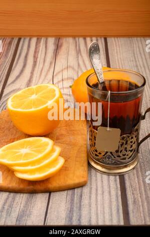 Tea in a faceted glass in a vintage Cup holder, sliced lemon on a Board on a wooden background. Close up Stock Photo