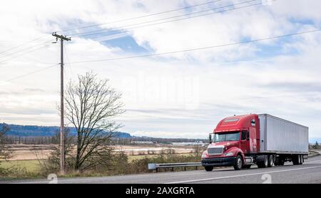 Big rig long haul red diesel semi truck with high cab configuration for improve aerodynamics transporting cargo in loaded dry van semi trailer running Stock Photo