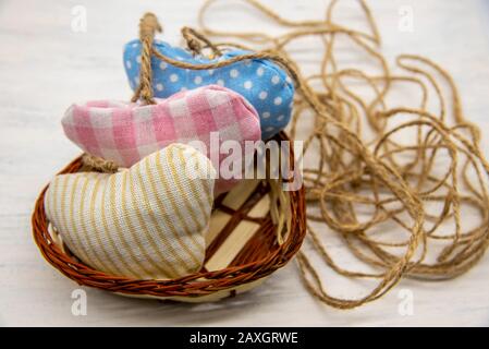 Hearts sewn from scraps in a wicker basket on a light wooden background. A coarse jute thread is twisted nearby. Stock Photo