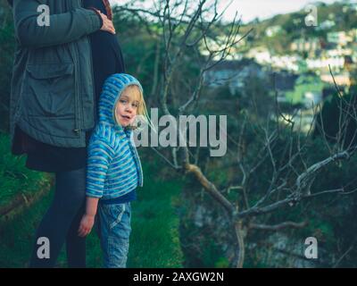 A young pregnant woman is standing in her garden with her preschooler on a winter day Stock Photo