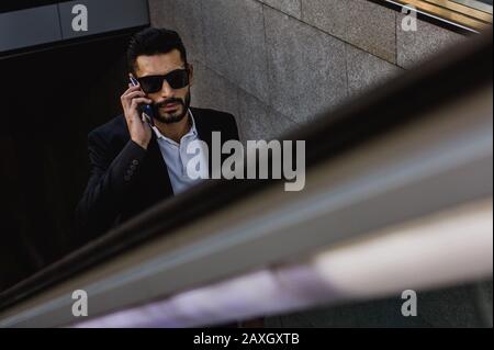 Businessman commuting, with his smartphone on escalators Stock Photo