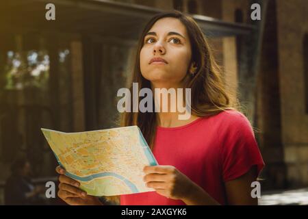 Tourist woman searching in a city map looking for a place in a urban background. Young traveler erasmus student girl lost Stock Photo