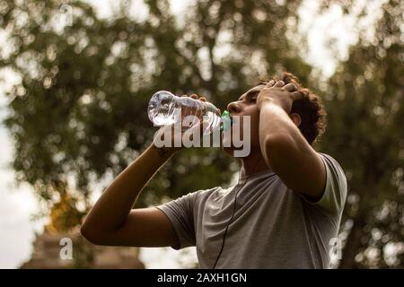 Runner drinking water. Exhausted latin young man with bottled water after workout