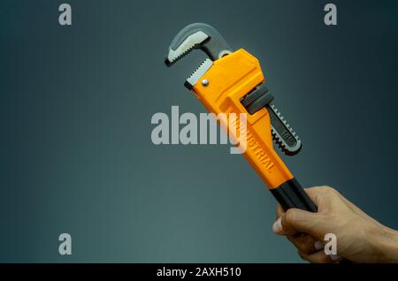 Plumber hand holding handle of chrome pipe wrench isolated on dark background. Metal monkey wrench for plumber. Mechanic tools. Hardware for fix and Stock Photo