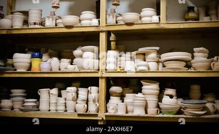 many different pottery standing on the shelves in a pottery workshop. Low light Stock Photo