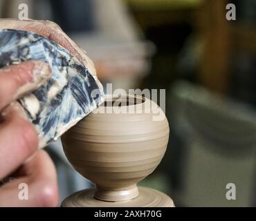 Potter makes a pretty small vase from clay, using the tool for surface leveling close-up macro. Space for text. Stock Photo