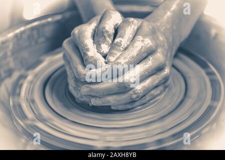 Old vintage photo. Master potter folded together hands sculpts a clay product on a potter's wheel. Hand skin stained with clay and wet Stock Photo