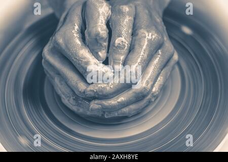 Old vintage photo. Master potter folded together hands sculpts a clay product on a potter's wheel. Hand skin stained with clay and wet Stock Photo