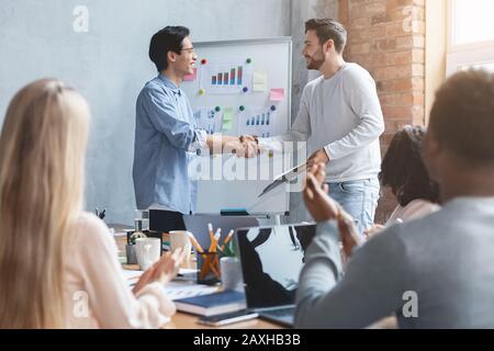 Young colleagues shaking each other hands during presentation Stock Photo