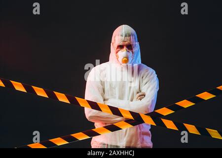 the epidemiologist in the zone of infection, surrounded by a warning tape. In the light of sirens. Stock Photo