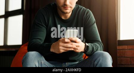 Guy Using Mobile Phone Sitting In Chair Indoor, Panorama, Cropped Stock Photo