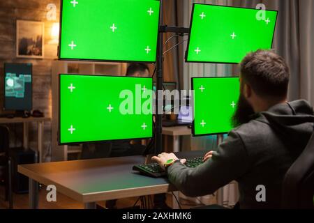 Bearded hacker spreading a virus using computer green screens. Stock Photo