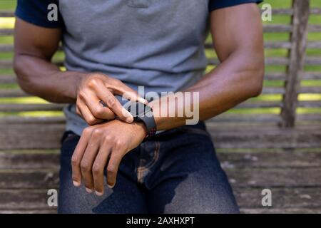 Young man sitting on a bench and using his smart watch Stock Photo