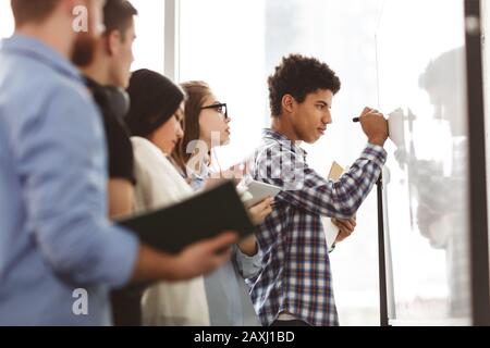 Afro guy writing algebra equations on whiteboard in classroom Stock Photo