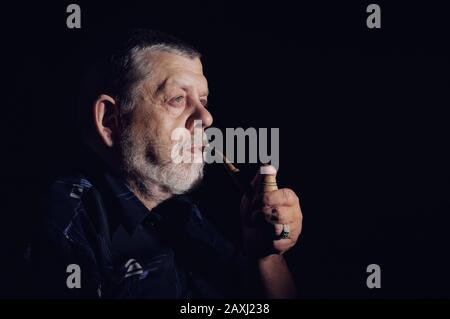 Nice dramatic portrait of senior smoking tobacco pipe in darkness Stock Photo