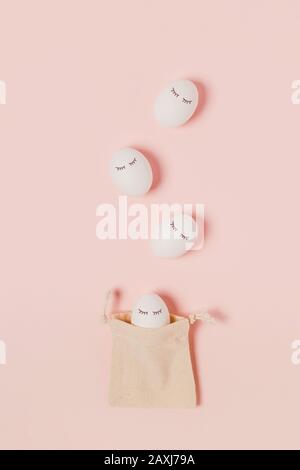 Happy Easter. White eggs with painted eyes in the rag bag and pink background. Flat lay, top view, copy space. Stock Photo