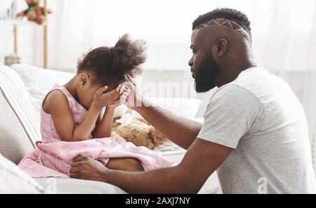 African father comforting little crying girl at home