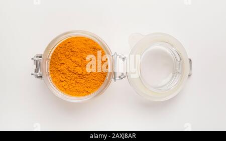 Turmeric powder in glass jar against white background Stock Photo