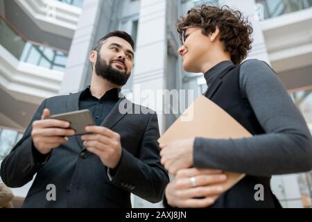 Below view of young ambitious business partners in formalwear discussing web project using smartphone in office Stock Photo