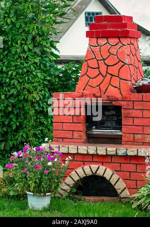 Landscaping in the garden. Red brick barbecue stove. Outdoor stone stove with grill. Summer outdoor activities. Close up, vertical. Stock Photo