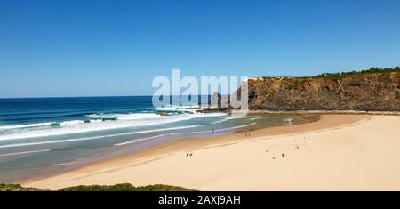 Coastline view of headlands and bay with wide sandy beach, surfer and a few sunbathers, Praia de Odeceixe, Algarve, Portugal, Southern Europe Stock Photo