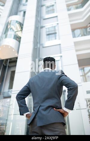 Rear view of Black man in jacket standing with hands on hips in modern business center Stock Photo