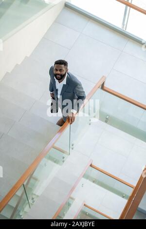 Above view of smiling young Afro-American businessman with beard carrying briefcase and moving up stairs in office center Stock Photo