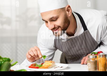 Chef Plating Roasted Salmon Steak And Decorating Dish In Kitchen Stock Photo