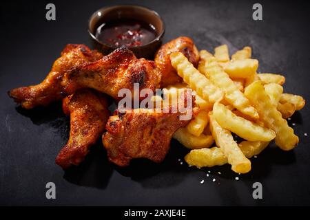 Close up on crispy spicy grilled chicken wings with chili dip on the side and a serving of oven baked crinkle cut potato chips for menu advertising Stock Photo