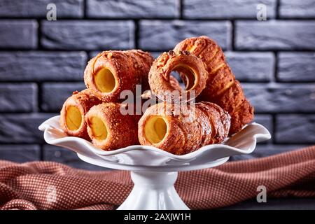 Hungarian chimney cake or kurtos kalacs - sweet rolled dessert served on a white standing plate on a dark concrete background in front of a black bric Stock Photo