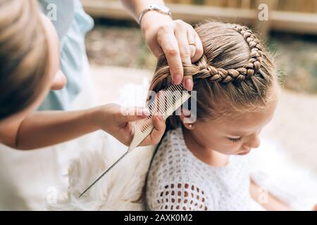 Mother does hair braid to her daughter, close up photo. Stock Photo