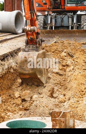 A road service excavator digs a trench on the roadway to replace old concrete blocks with new wells and sewer pipes. Stock Photo