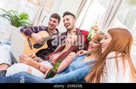 Group of teenagers having fun at home using laptop and playing guitar in living room - Group of people enjoying time together Stock Photo