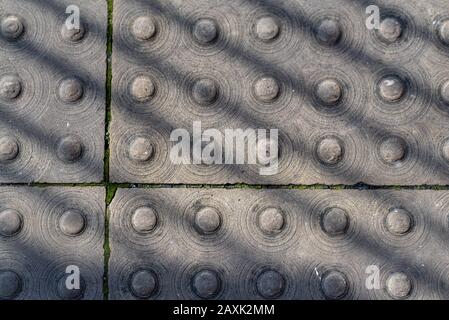 Grey paving slabs with small circle detail, sunlight and shadow.  Abstract background.  Ipswich, Suffolk, UK Stock Photo