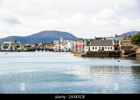 Waterfront of a coastal town on a cloudy spring day. A mountain is visible in background. Stock Photo
