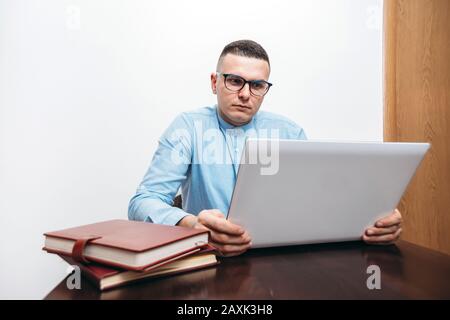 Man with glasses holding laptop in the office with books on the desk Stock Photo