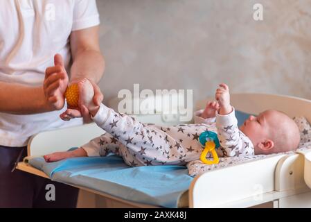 Dad is caring for the baby. A father gives his child a ball foot massage. Stock Photo