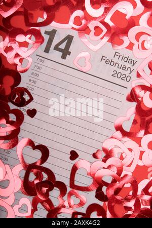 Calendar page open to Valentine's Day 2020 surrounded by shiny hearts on a red background Stock Photo