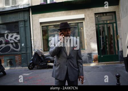 Man in grey suit and hat holding mobile phone to ear, smoking - street photo Stock Photo