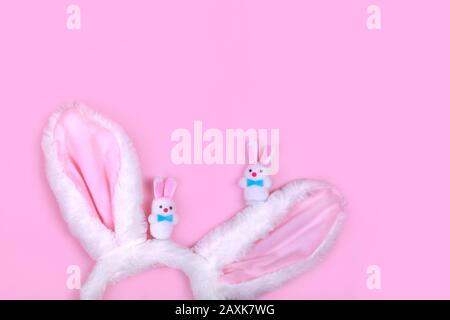 Happy Easter concept. Furry bunny ears costume toy isolated on trendy pink background with small fluffy rabbits toys. Simple minimalist flat lay Stock Photo