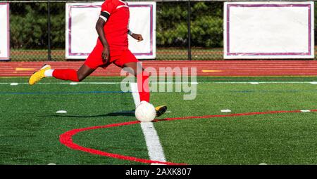 An African American high school soccer player in a red uniform is about to kick the soccer ball during a free kick at a game. Stock Photo