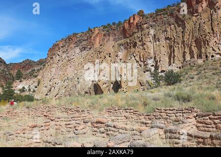 Part of the Tyuonyi ruins of the ancestral Pueblo peoples an unidentifiable hikers by the cliffs along the main loop trail in Frijoles Canyon at Bande Stock Photo